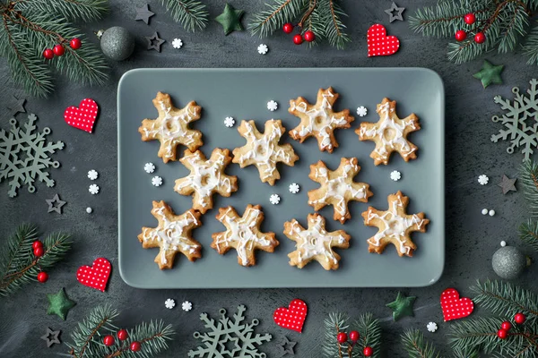 Gri tabakta kar taneleri şeklinde bir tabak Noel kurabiyesi. Düz zemin üzerinde yatıyordu. Xmas ağaç dalları, kalpler, böğürtlenler ve yıldızlarla süslenmiş..