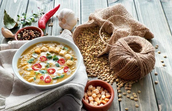 Spicy lentil soup with chili, garlic and onion on rustic wooden table. The soup is served with cream, chili, lemon, croutons and thyme leaves in white bowl, with ingredients all around. — Stock Image Spicy Lentil Soup Chili Garlic Onion Rustic Wooden Table Soup Royalty Free Stock Photos