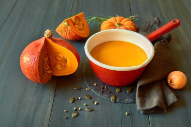 Balkabağı kremalı çorba, koyu ahşap üzerinde kırmızı diş minesi kabı.