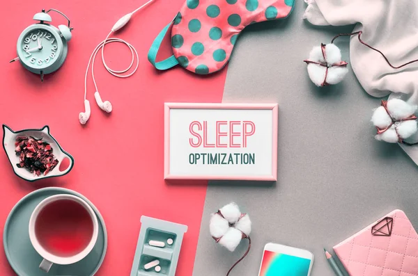 Healthy night sleep creative concept. Sleeping mask, alarm clock, earphones, earplugs, tea and pills. Split two tone orange coral and green background with palm leaves. Text "sleep optimization" in fr — ストック写真