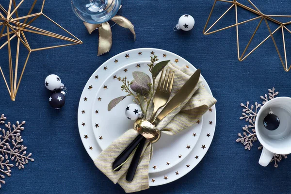 Christmas table setup with white plate and golden utensils and g