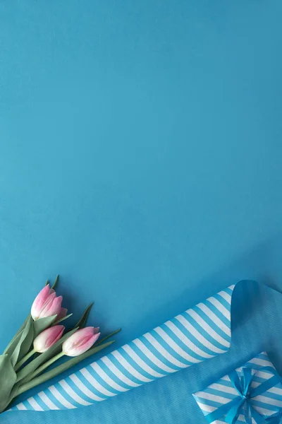 Blue background with pink tulips, stripy wrapping paper and gift — Stock Photo, Image