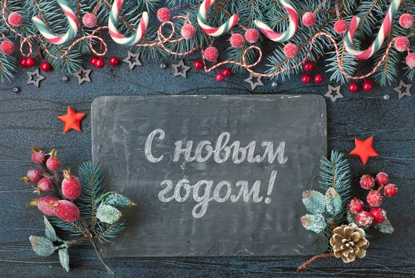 Happy New Year text in Russian language. Christmas background with fir twigs, red berries and candy canes with textured board on textured grey background, text space — ストック写真