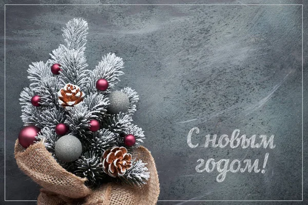 Happy New Year text in Russian language. Small Christmas tree in sackcloth decorated with red baubles and berries on dark textured background. — 스톡 사진