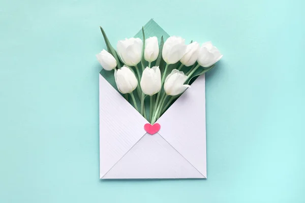 Tulipes blanches dans une enveloppe blanc-vert sur fond de papier menthe bleu — Photo