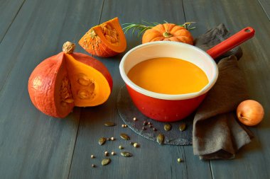 Balkabağı kremalı çorba, koyu ahşap üzerinde kırmızı diş minesi kabı.