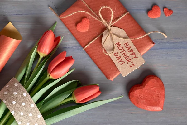 Regalo envuelto tulipanes rojos, papel de regalo y corazones decorativos en — Foto de Stock