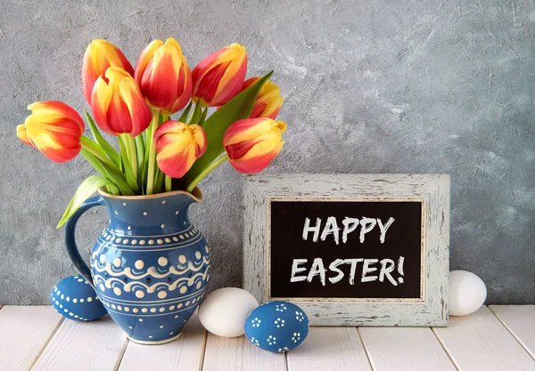 Tulipanes rojo-amarillos en jarra de cerámica azul con huevos de Pascua y un —  Fotos de Stock