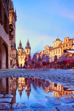 Prag 'daki Aziz Mary Tyn Kilisesi' nde yaz yağmurundan sonra su birikintisine yansıyan yansımayla Eski Şehir Meydanı 'na doğru yürüyen turistler görülüyor. Prag, Çek Cumhuriyeti.