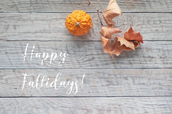 Hojas de otoño y calabazas, texto "Felices Fiestas". Puesta plana, vista superior de calabazas naranjas, mazorca de maíz y hojas secas en madera rústica . — Foto de Stock