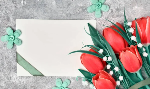 Saludos de primavera, cama plana con tulipanes rojos y tarjeta de papel en blanco — Foto de Stock