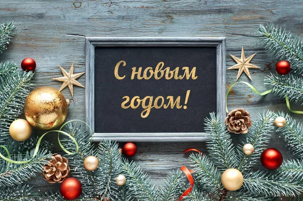 W År text på ryska. Grön, röd och gyllene jul bakgrund. Dekorerade grankvistar runt svart bräda på rustikt trä. Ovanifrån med kopieringsutrymme. — Stockfoto