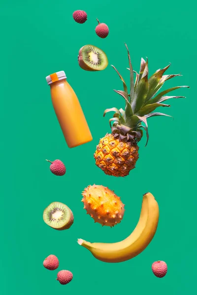 配上热带水果和绿色背景的橙色软糖瓶。 菠萝、猕猴桃、猕猴桃、荔枝和香蕉-异国情调水果、悬浮和维生素平衡. — 图库照片