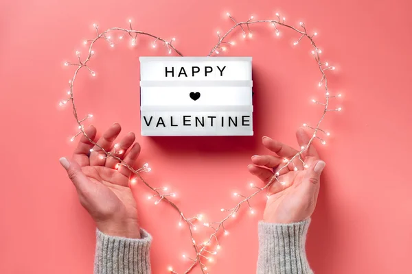 Valentine płaski leżał, widok z góry na różowe tło. LightBox z napisem "Szczęśliwych Walentynek". Lekka girlanda w kształcie serca trzymana w żeńskich dłoniach. Walentynki kreatywna koncepcja. — Zdjęcie stockowe