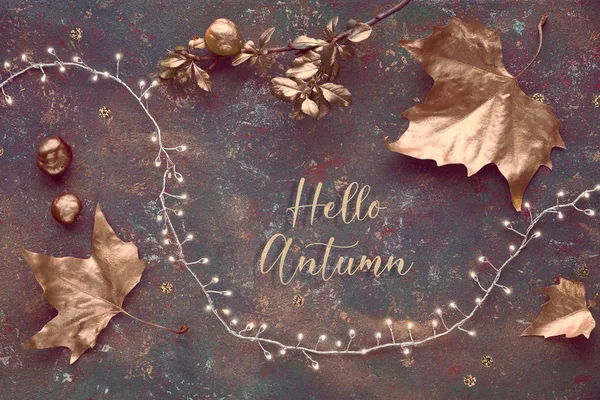 Autumn, creative panoramic flat lay. Top view of painted golden leaves, festive light garland on dark green textured background. Text "Hello Autumn" in gilded joined Italic script. — Stock Photo, Image