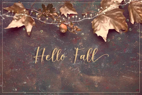Flat lay, top view with painted golden leaves, festive light garland on dark textured background. Text "Happy Fall" in gilded joined Italic script. Happy Fallidays! — 스톡 사진