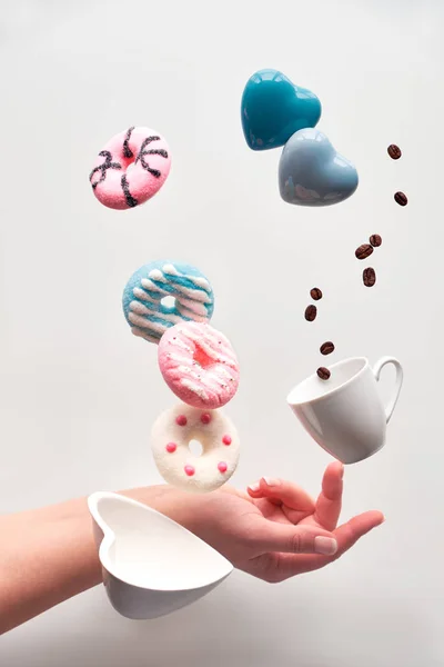 St. Valentine concept, levitation of doughnuts above heart shaped bowl. Coffee beans fly in espresso cup. Hand balancing coffee cup on finger. Creative levitation of sweet food with coffee.