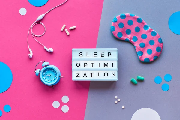 Text "Sleep optimization" on lightbox. Sleeping mask in polka dots, small alarm clock, earphones and earplugs, capsules and pills. Flat lay, top view, split two tone pink and green background. — Stock Photo, Image