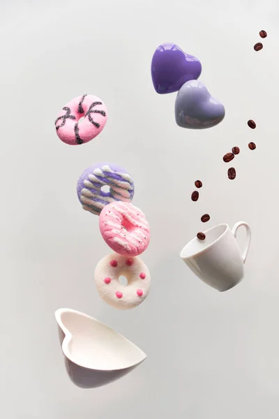 Sevgililer günü konsepti, kalp şeklindeki çöreklerin havaya kaldırılması. Kahve çekirdekleri espresso bardağında uçar. Açık gri renkli yaratıcı arkaplan. — Stok fotoğraf