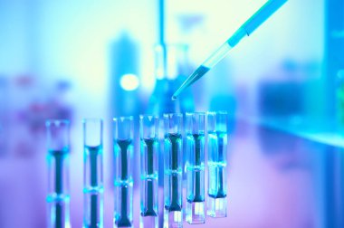 Scientific background in vibrant neon colors, purple, blue and turquoise. Pharma, biotech, protein analysis. Spectrophotometer quvettes on a reflective surface, copy-space., focus on pipette tip.