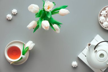 Mother;s day celebration, flat lay on table set for tea. Trendy modern flat lay, top view. Tea pot, sweets and white tulips on light grey. Sweet marshmallows tasty snack.