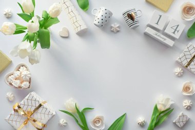 Spring flat lay, top view with white tulips, flowers, geometric decorations - coffee cups, gift boxes wrapped in hexagon paper with gold line pattern, stone blackboard. Text space, copy-space.