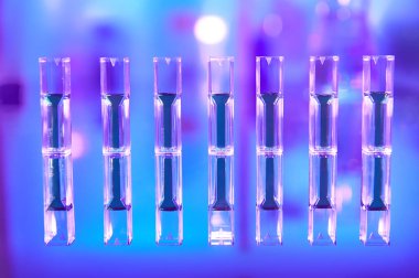 Scientific background in vibrant neon colors, purple, blue and turquoise. Pharma, biotech, protein analysis. Spectrophotometer quvettes on a reflective surface, copy-space.
