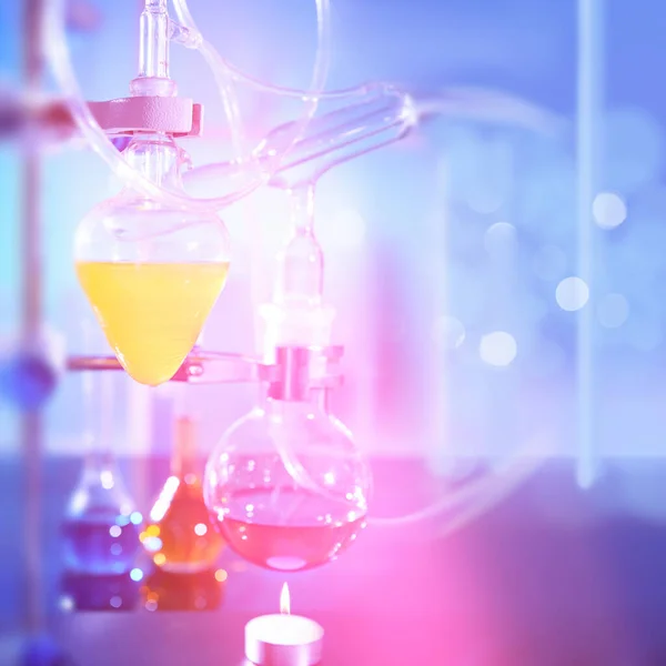 Reaction in progress in organic chemistry lab, distillation glassware, laboratory glass equipment. Futuristic neon lights, bold vibrant purple, pink, blue and turqiouse lights. Experiment in progress.