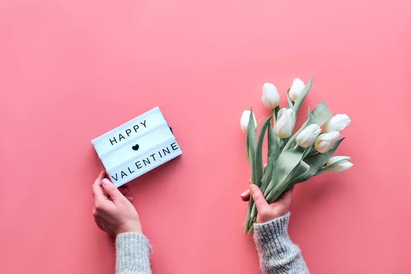 St Valentine's day pink background. Woman hands hold bunch of white tulips, flowers. Lightboard in heart shape with illuminated lights. Flat lay, top view, minimal trendy Valentine design concept. — ストック写真