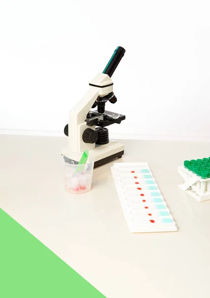 Equipment for microscopy, light microscope, tray of microscopic tissue samples, plastic tubes with reagents and forceps on white laboratory bench, copy-space. Study, training or school biology setup.