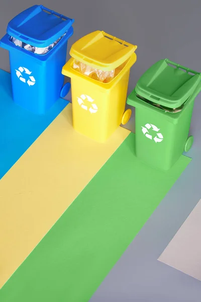 Trzy kolorowe kosze na śmieci, obraz izometryczny na geometrycznym wielowarstwowym tle papieru. Znak recyklingu na niebieskich, żółtych i zielonych pojemnikach. Oddzielenie odpadów, ograniczenie ilości odpadów zmieszanych i recykling tworzyw sztucznych — Zdjęcie stockowe