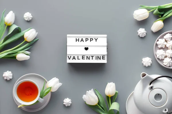 Happy Valentine tekst op lichtbord met vakantie decoraties. Theepot, snoepjes en witte tulpen op zilvergrijze ondergrond. Trendy moderne flat lay, bovenaanzicht — Stockfoto