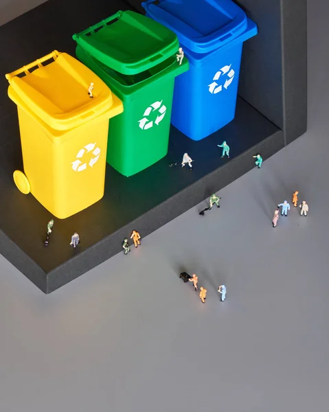 Miniature people, workers around three color coded recycle bins, isometric projection with copy-space. Recycling sign on the bins, blue, yellow and green. Waste separation concept, eco friendly life.