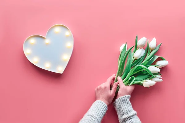 Springtime flat lay, female woman hands holding bunch of white tulips, Spring flowers. Lightboard in heart shape with illuminated lights. Flat lay, top view, Mother's day or Valentine. — ストック写真