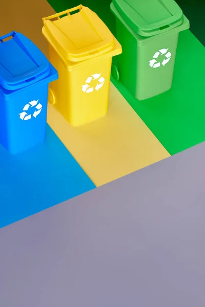 Three color coded recycle bins, isometric projection on layered paper background with copy-space. Recycling sign on the bins, blue, yellow and green. Waste separation to reduce plastic in landfills. — 图库照片