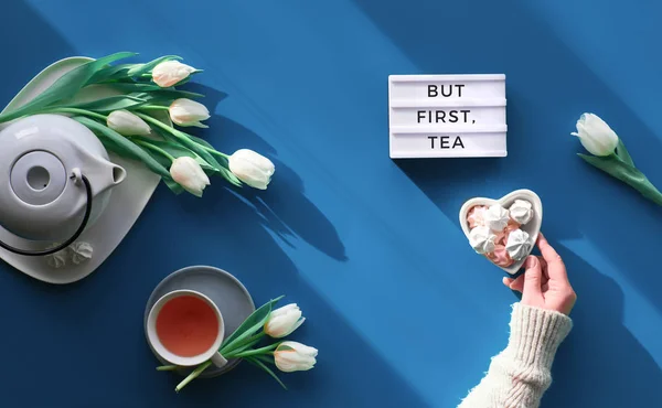 Happy Valentine day, Mother's day or other Spring celebration flat lay. Female hand with heart shape bowl with sweets.. Tea cup, tea pot and white tulips on tale, trendy classic blue background — Stok fotoğraf