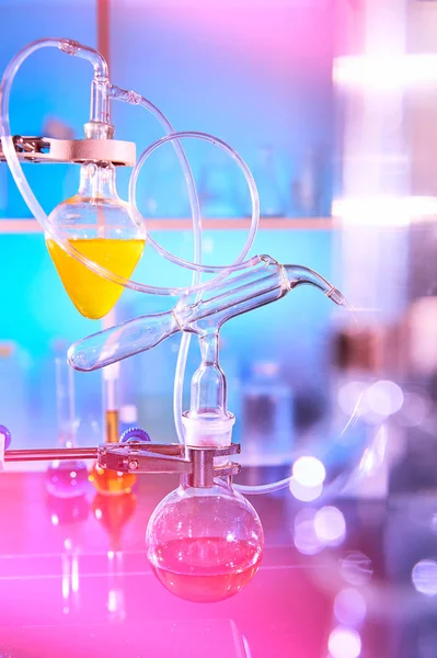 Reaction in progress in organic chemistry lab, distillation glassware, laboratory glass equipment. Futuristic neon lights, bold vibrant purple, pink, blue and turqiouse lights. Reaction in progress.