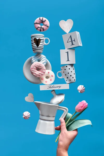 Día de San Valentín fondo divertido en menta azul. Fecha 14 de febrero en el calendario de madera con tazas de café, tulipán, rosquillas y malvaviscos. La mano femenina sostiene la pirámide de equilibrio . — Foto de Stock