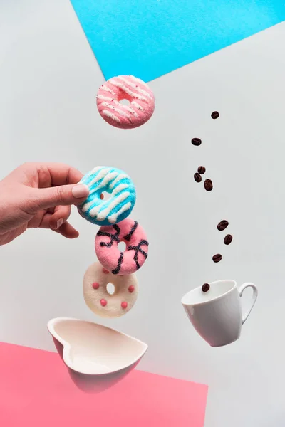 St. Valentine concept, levitation of doughnuts above heart shaped bowl. Coffee beans fly in espresso cup. Hand catching pink doughnut. Creative geometric background in pink and light grey colors. — 图库照片