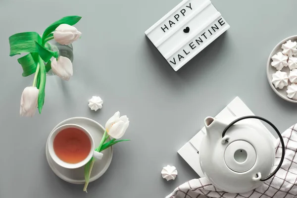 Geometric panoramic flat lay with hands. Cup of black tea, tea pot, sweets and white tulips on grey with lightboard. Text Happy Valentine day on the light board. Geometric top view. — ストック写真