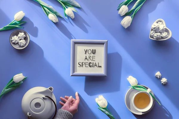 Spring geometric flat lay. Female hand hold frame with text You are special. Tea cup, pot, sweets and white tulips on pale purple. Mothers day, international women day 8 March or your Mama birthday. — Stok fotoğraf