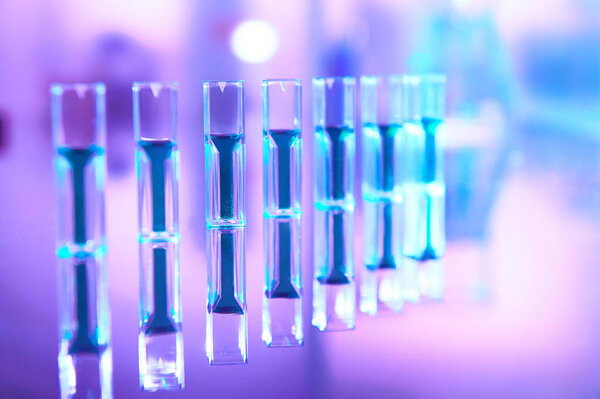 Scientific background in vibrant neon colors, purple, blue and turquoise. Pharma, biotech, protein analysis, protein concentration measuring. Spectrophotometer quvettes with reflection, text space.