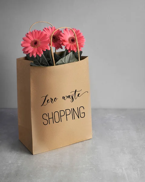 Korallenfarbe rosa Gerbera Gänseblümchen Blumen und Bastelpapier Einkaufstüten auf grau neutralem Hintergrund, Frühlingsverkauf Konzept Bild mit Text "Zero Waste Shopping" auf der Tasche — Stockfoto