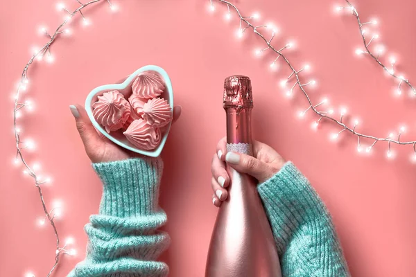 Valentine Draufsicht auf rosa Hintergrund. Lichterkranz, Frauenhände mit metallisch rosa Champagner und Marshmallows in Herzschale. st. valentinstag 14. februar einfarbig flach lag. — Stockfoto