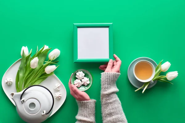 Spring celebration flat lay. Mothers day, Valentine, international women day 8 March, birthday, other special occasion. Tea pot, tea cup and white tulips, sweets. Hands hold blank frame, copy-space. — 图库照片