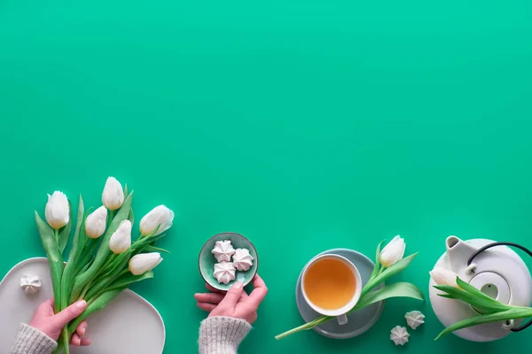 Geometric panoramic flat lay with hands. Cup of black tea, tea pot, sweets and white tulips on green with copy-space. Valentine day, Mother's day, international women day March 8. Modern trendy top vi — ストック写真