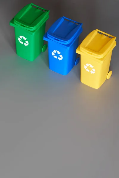 Tre bidoni di riciclo codificati a colori, immagine isometrica su carta grigia, copia-spazio. Segnale di riciclaggio sui bidoni, blu, giallo e verde. Separazione dei rifiuti per ridurre i rifiuti misti e riciclare carta e plastica . — Foto Stock