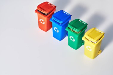 Dört renk kodlu geri dönüşüm kutuları, geometrik gökkuşağı kağıdının arka planında fotokopi uzayı ile izometrik projeksiyon. Çöp kutularındaki geri dönüşüm işareti - kırmızı, mavi, sarı ve yeşil beyaz üzerinde izole edilmiş. Atık ayırma