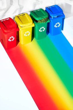 Four color coded recycle bins, isometric projection on geometric rainbow paper background with copy-space. Recycling sign on the bins - red, blue, yellow, green. Waste separation concept background.