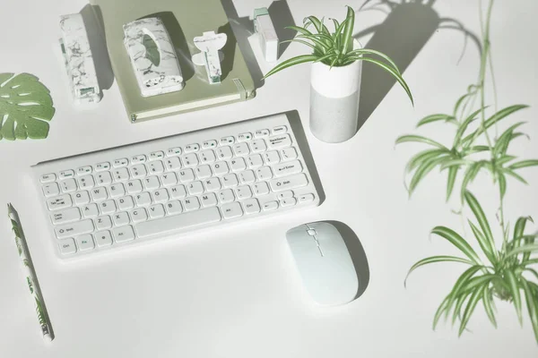 Concept workspace background with modern office supplies in white, green, marble. Isometric projection, geometric lay with exotic leaves. Notebook, stapler, keyboard, mouse and office things.